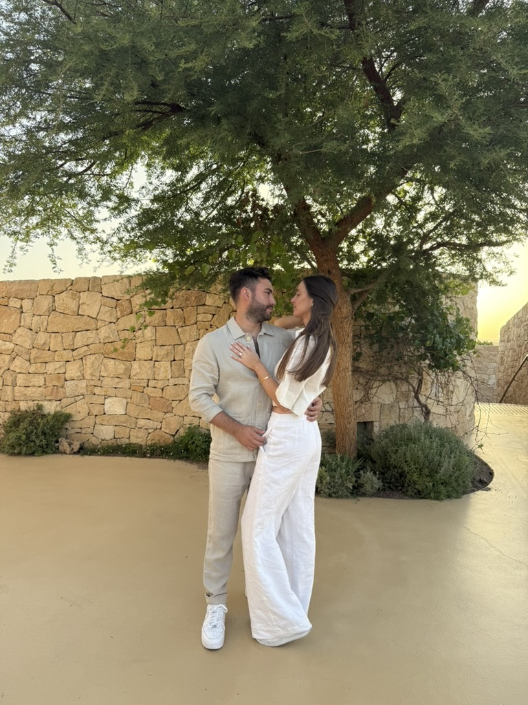 Joshua and Gabriella kissing beneath a tree beside a stone wall at dusk