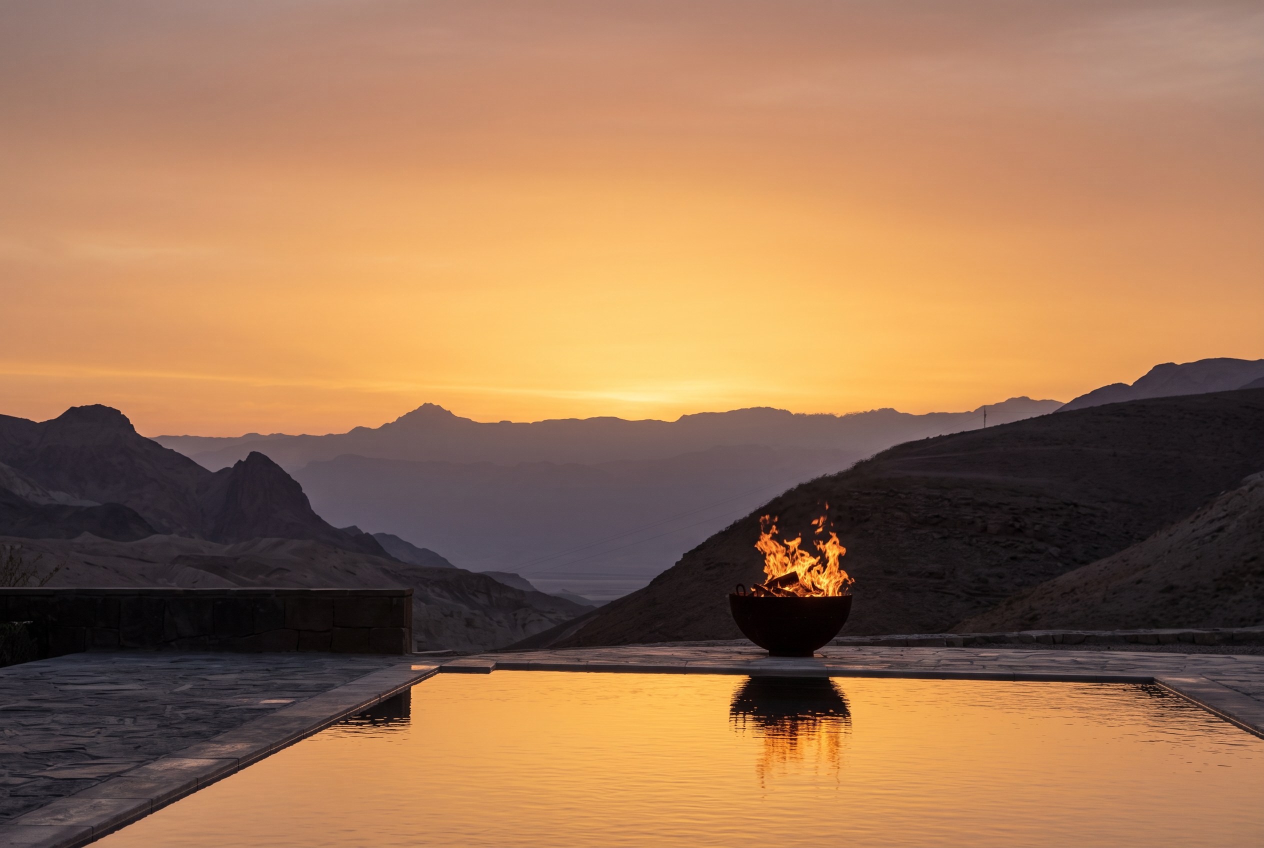 A fire bowl glowing beside the pool at sunset